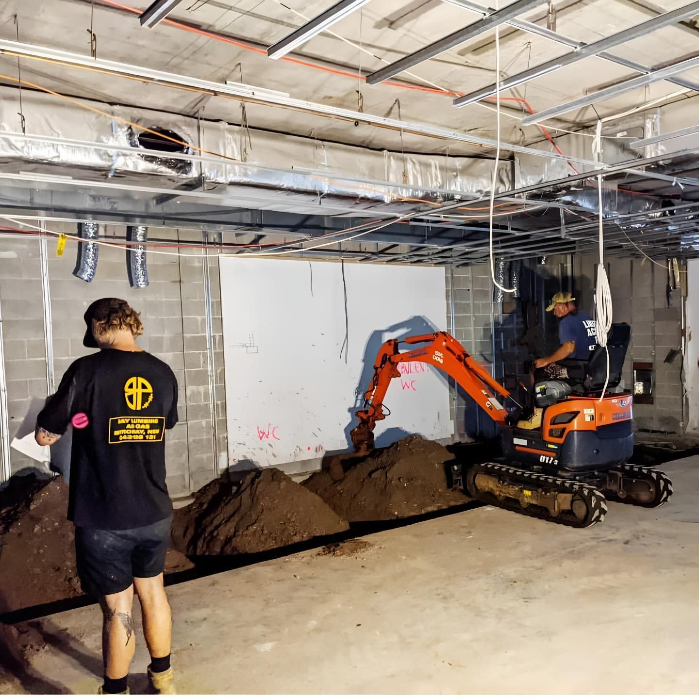A Man is Standing Next to a Small Excavator in a Basement — Limited Access Excavation In Suffolk Park, NSW