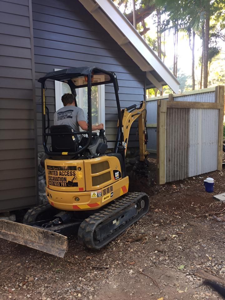 A Small Yellow Excavator is Parked in Front of a House — Limited Access Excavation In Suffolk Park, NSW