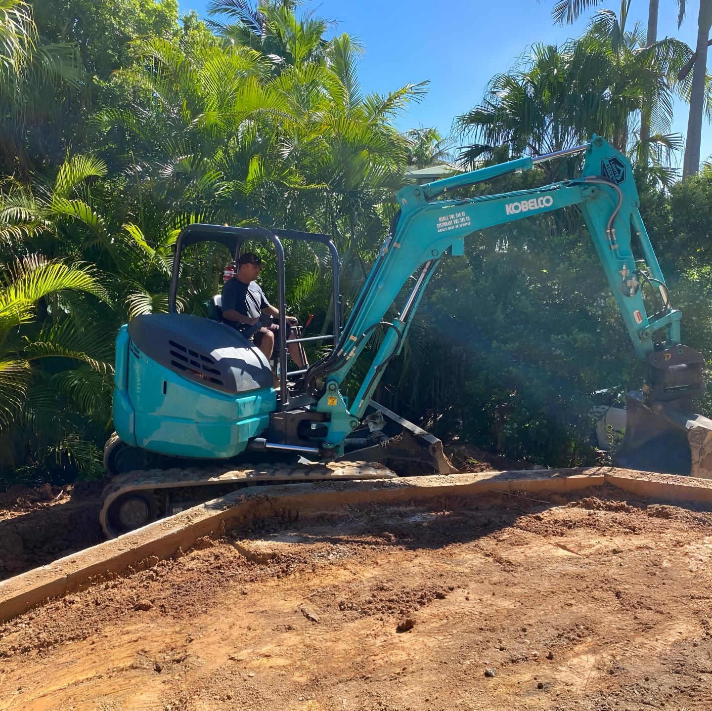 A Man is Driving a Kobelco Excavator on a Dirt Road — Limited Access Excavation In Yamba, NSW