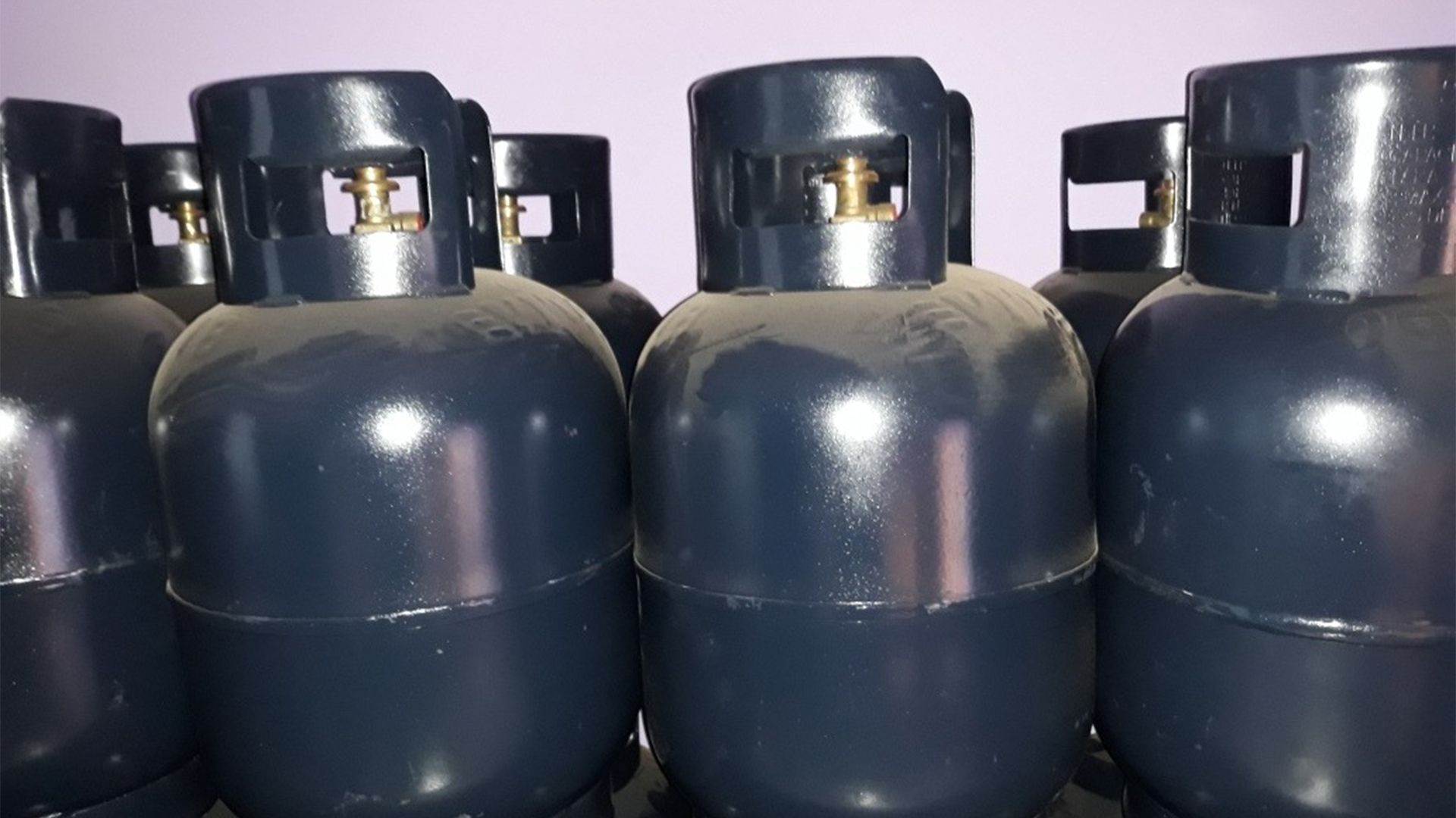 Tanques de propano azules, de cerca, alineados sobre un fondo violeta claro.