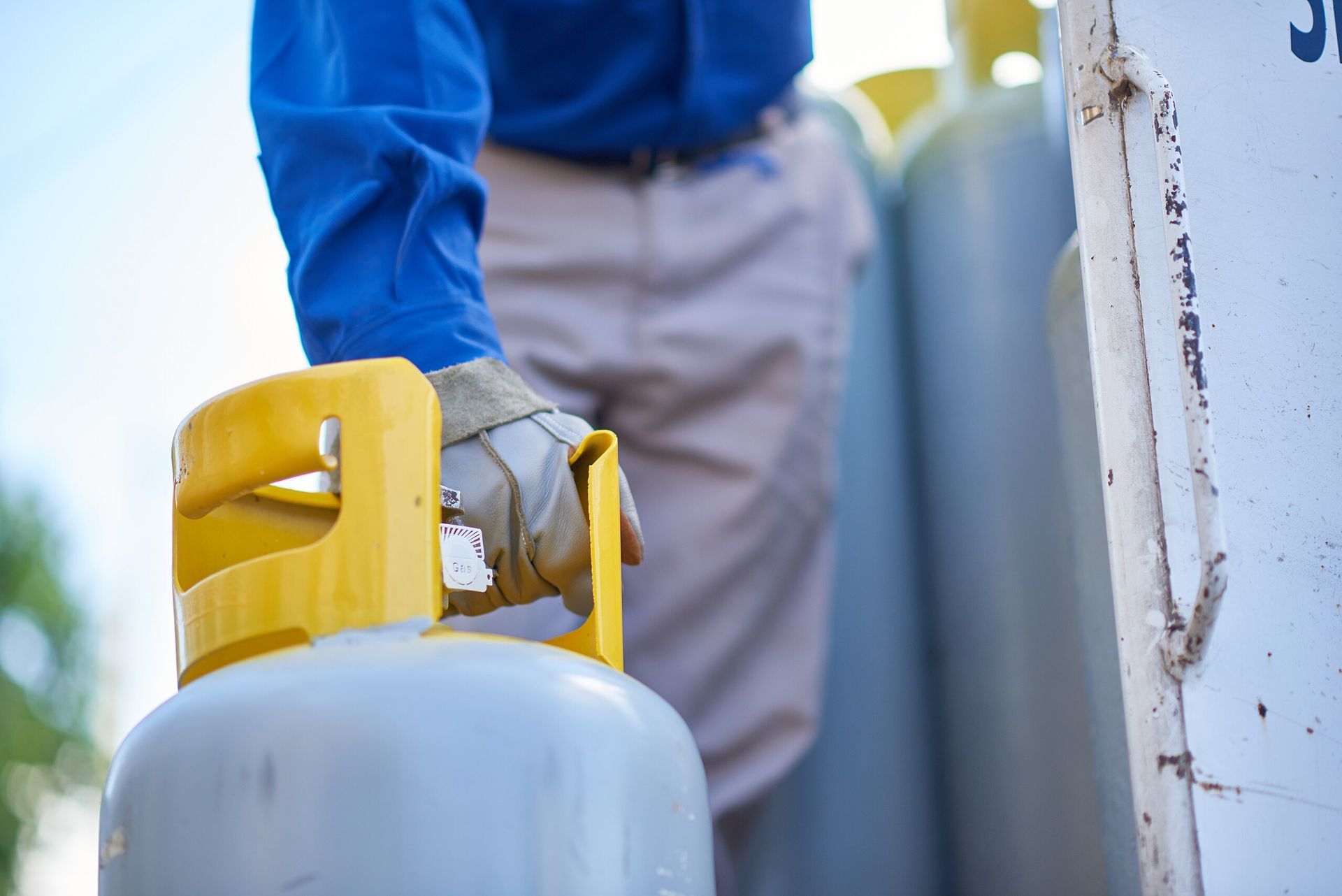 Persona con guantes manipulando un tanque de propano amarillo. Se ven otros tanques.