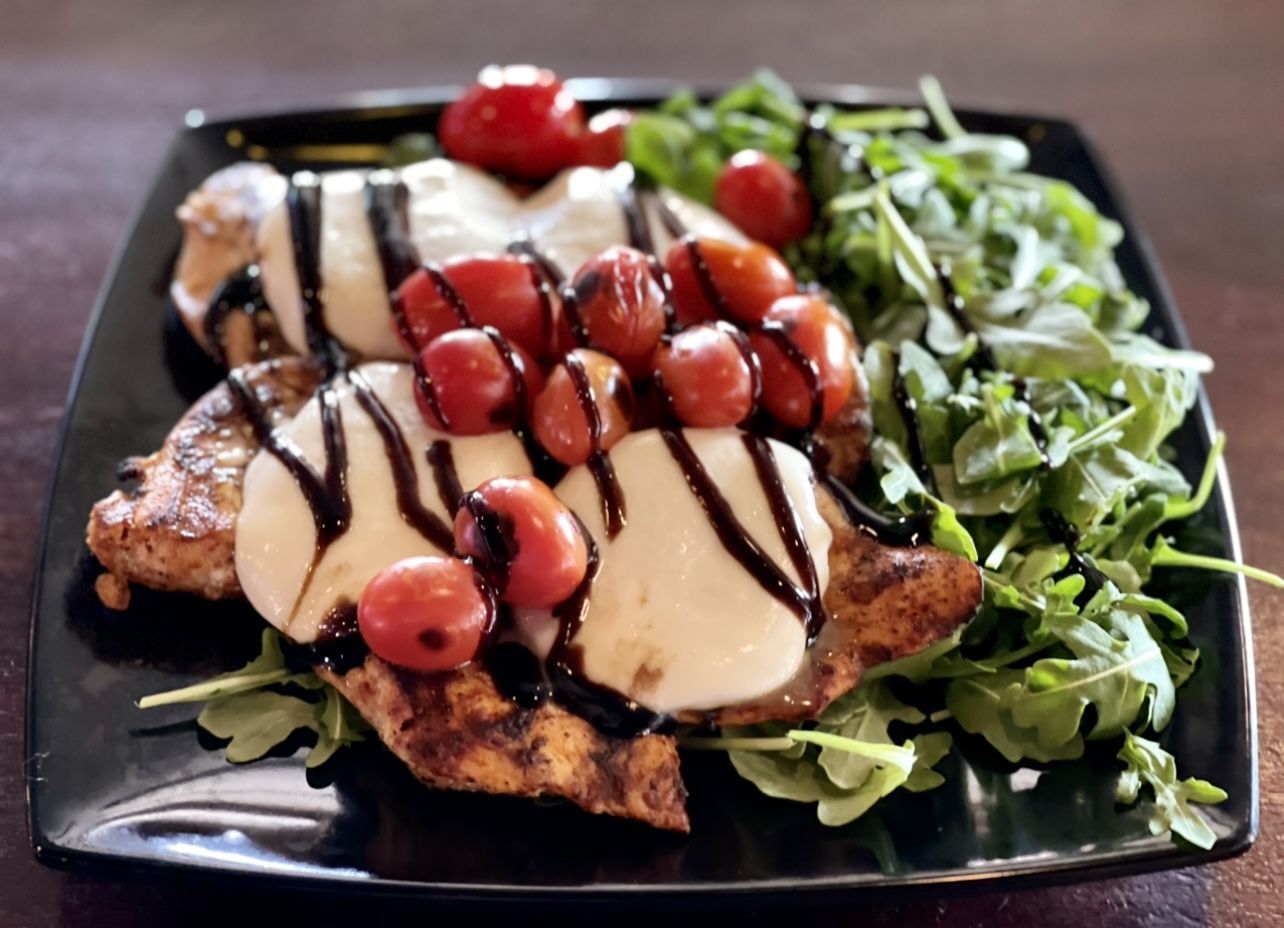 A black plate topped with chicken and tomatoes on a table.