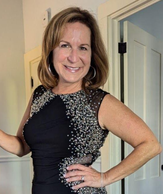 Woman with white hair, glasses, and black shirt smiling outdoors.