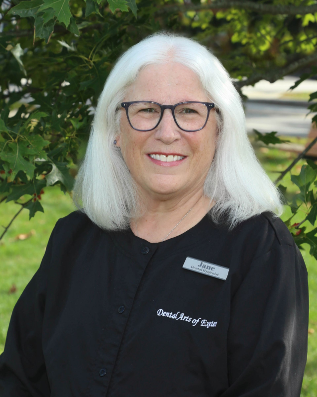Woman with white hair, glasses, and black shirt smiling outdoors.