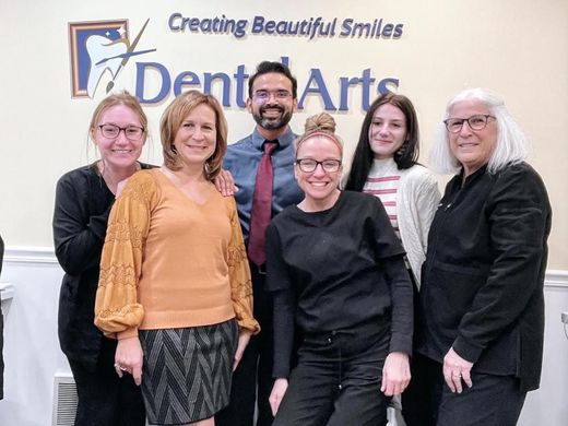 A group of people are posing for a picture in front of a dent arts sign.