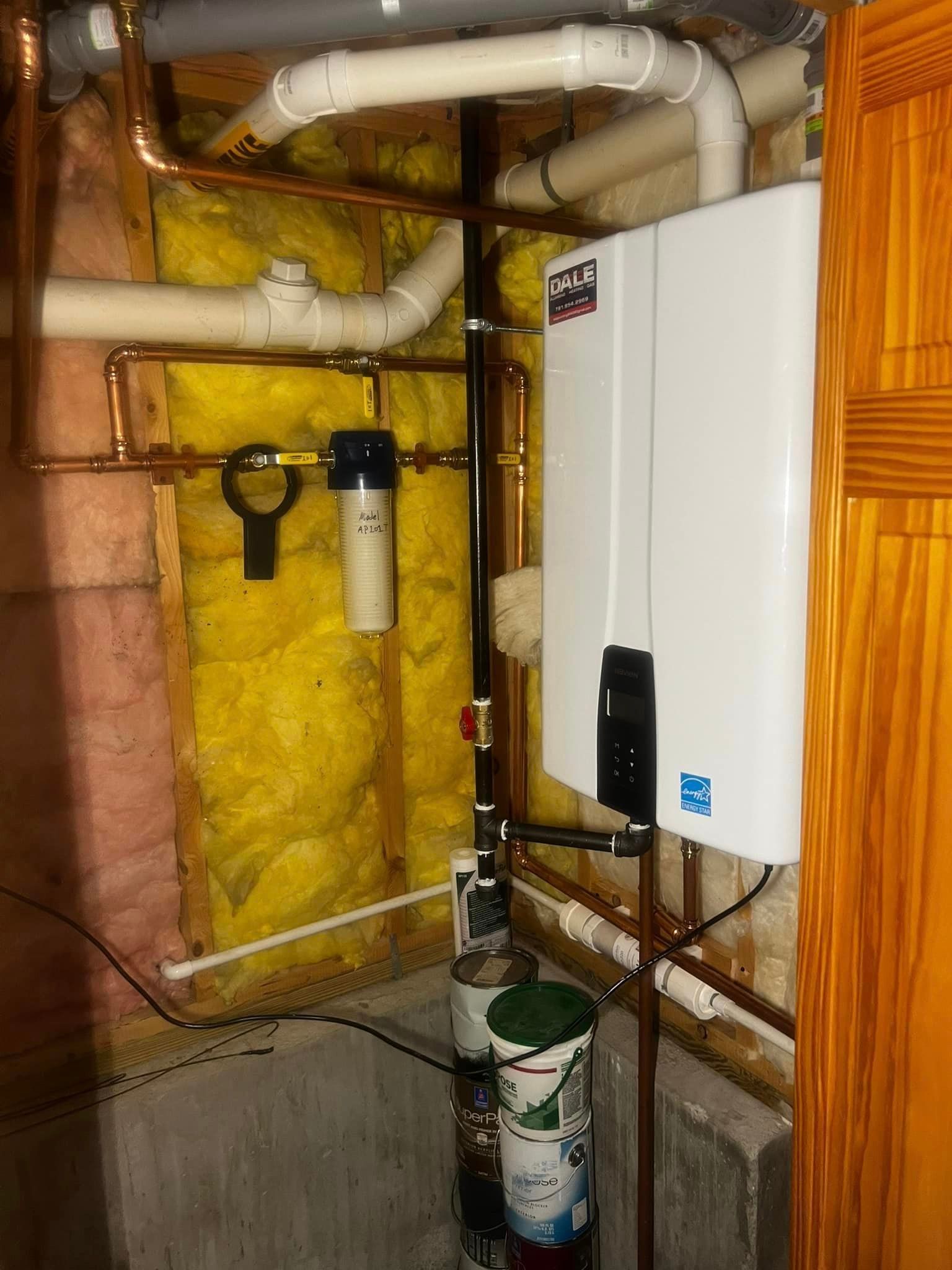 a white water heater is sitting in a room with pipes and insulation .