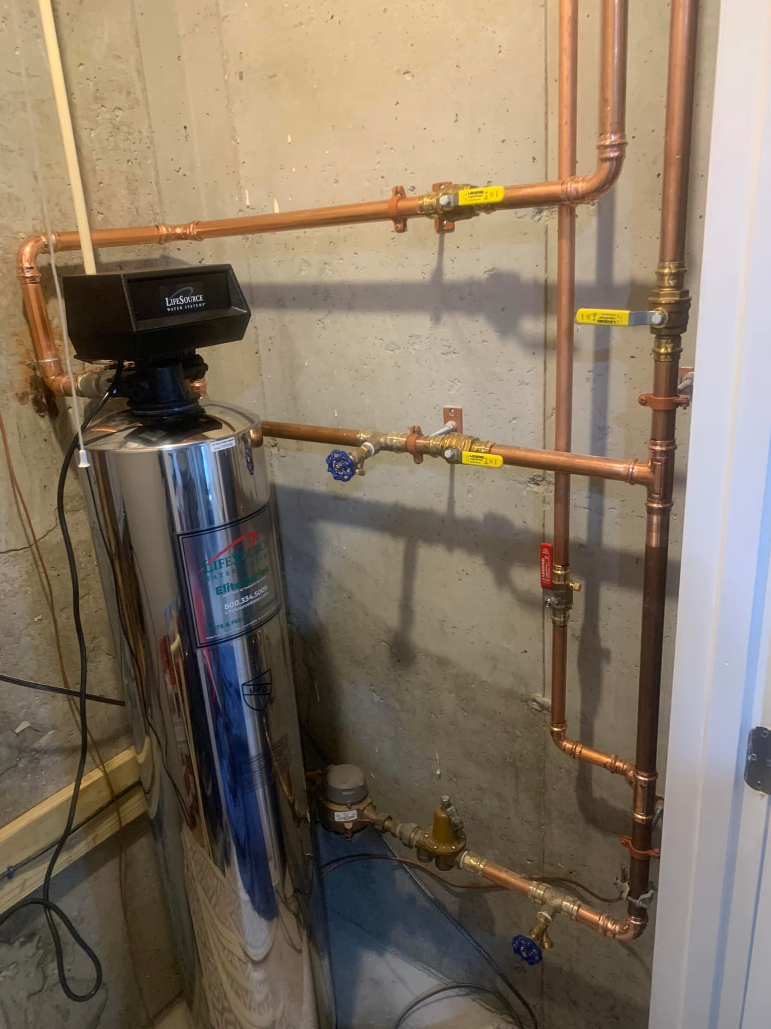 a water heater is sitting in a room next to copper pipes .