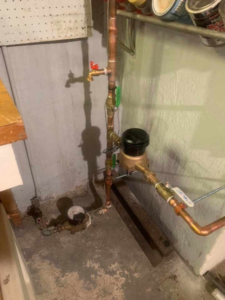 a water meter is sitting next to a copper pipe in a basement .