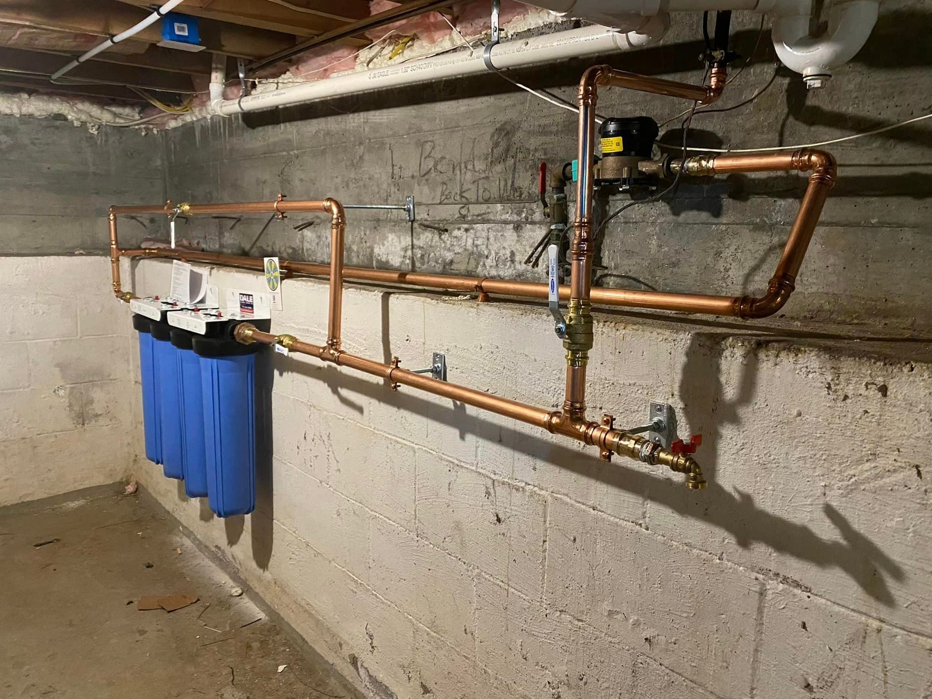 a basement with copper pipes and a water filter hanging on the wall .