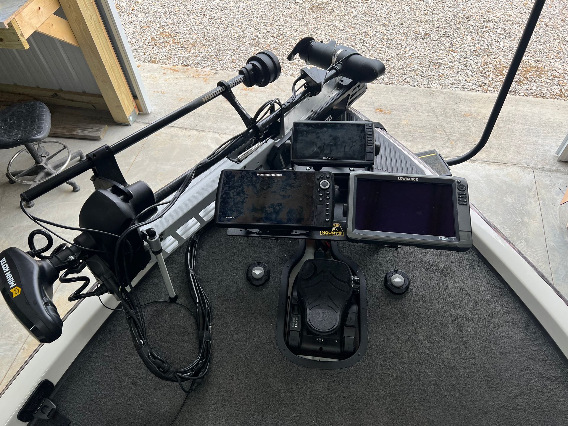 Fishing boat dashboard with electronic screens, trolling motor, and foot pedal.