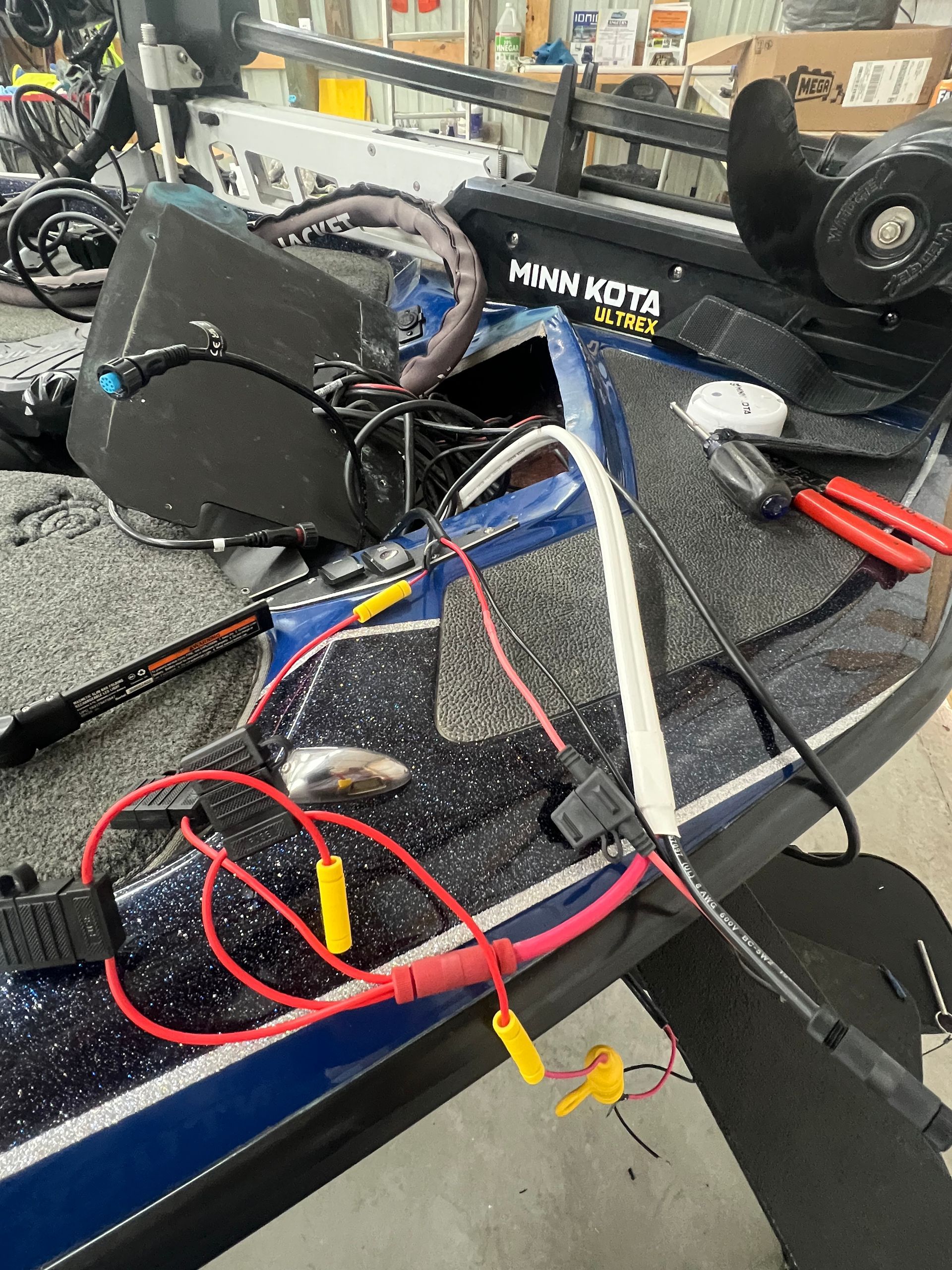 A person working on the electrical components of a blue and black fishing boat, with tools and wires visible.