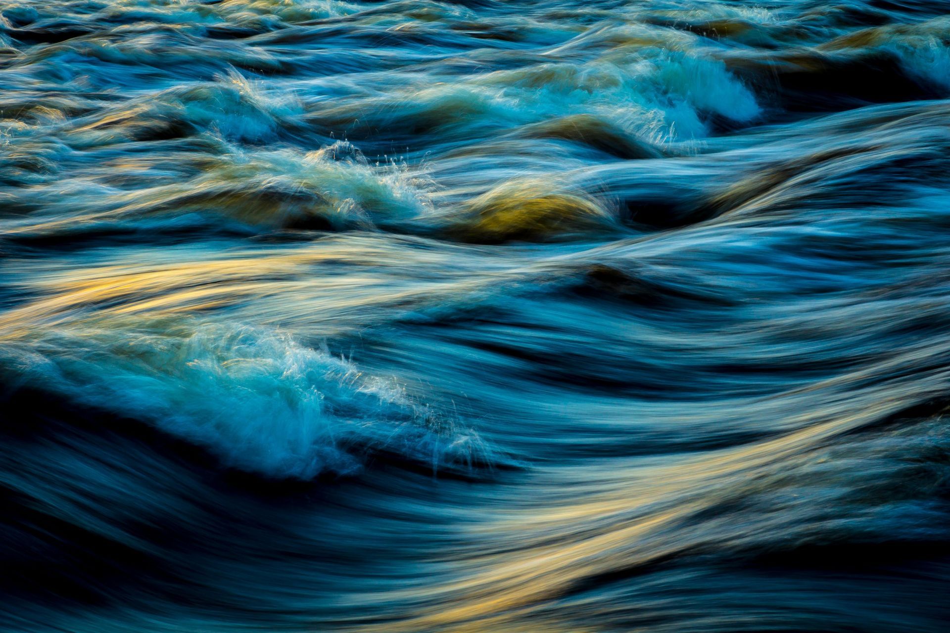 Waves of blue water, with white foam and golden highlights, creating a dynamic, fluid scene.