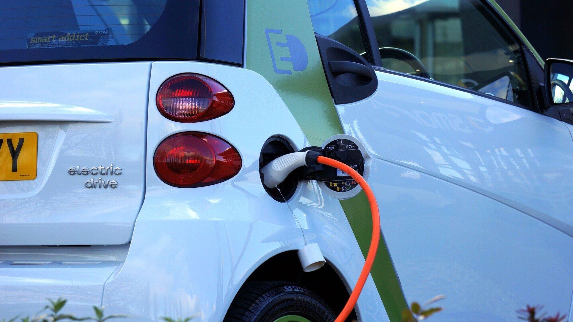 A white electric car is being charged with an orange cord.