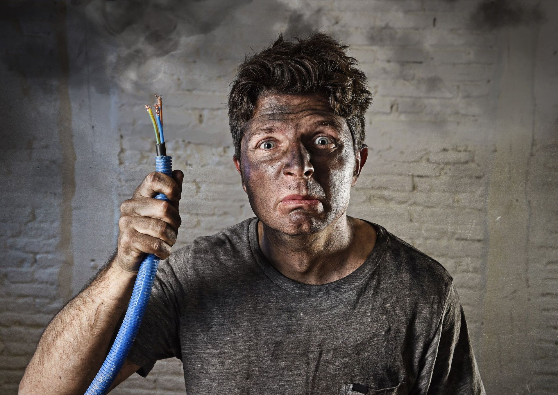 man covered in soot with smoking hair holding a cord with exposed wires