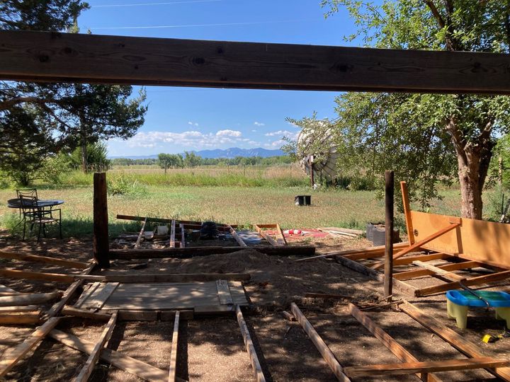 Construction site of a deck frame with a scenic field and mountains in the background under a bright blue sky.