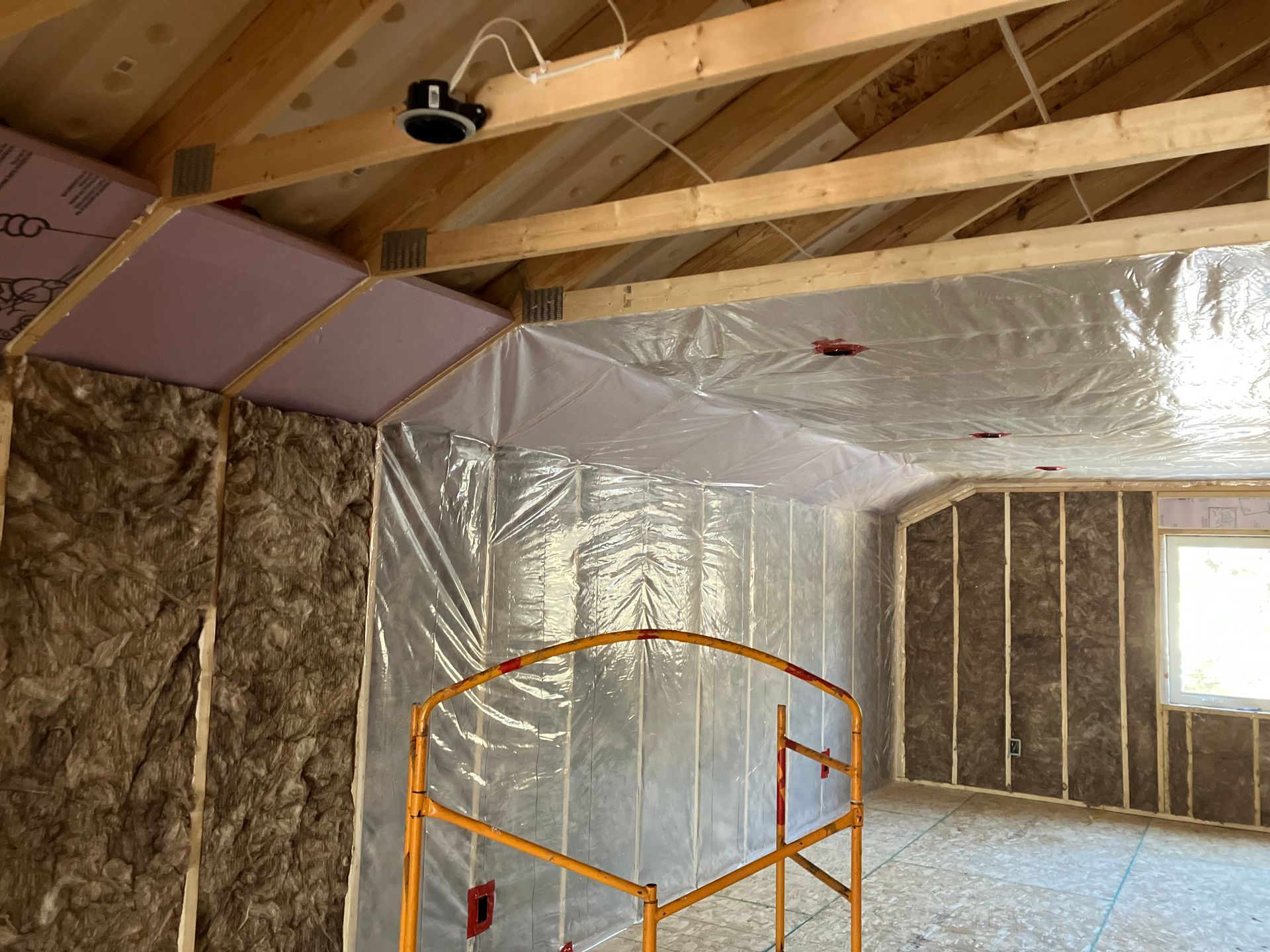 Interior of a room under construction, insulated with spray foam between wooden studs and rafters.