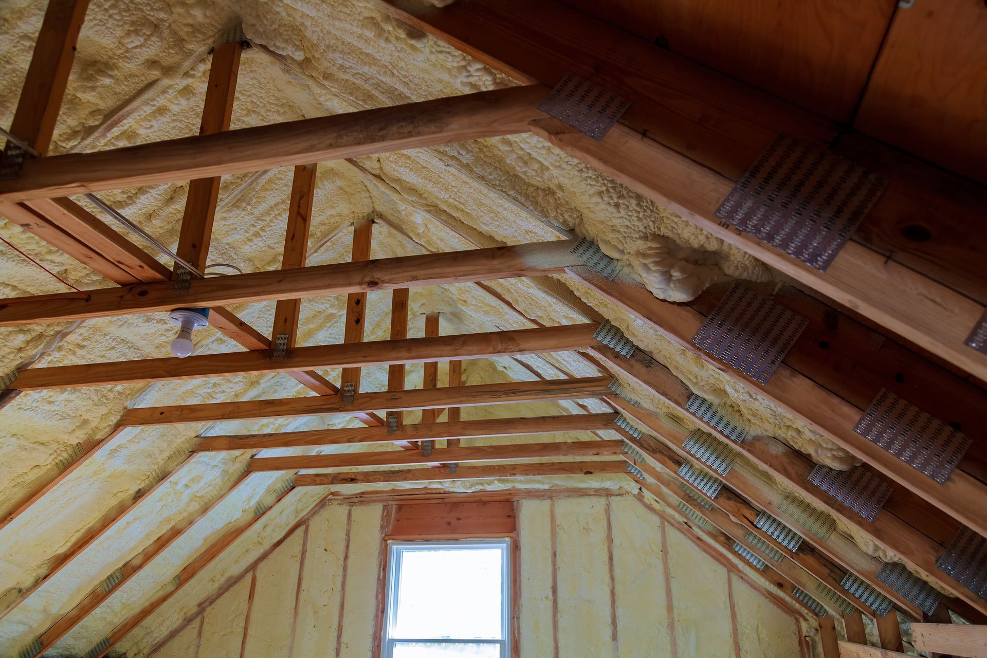 Attic rafters with spray foam insulation; wooden beams, small window.
