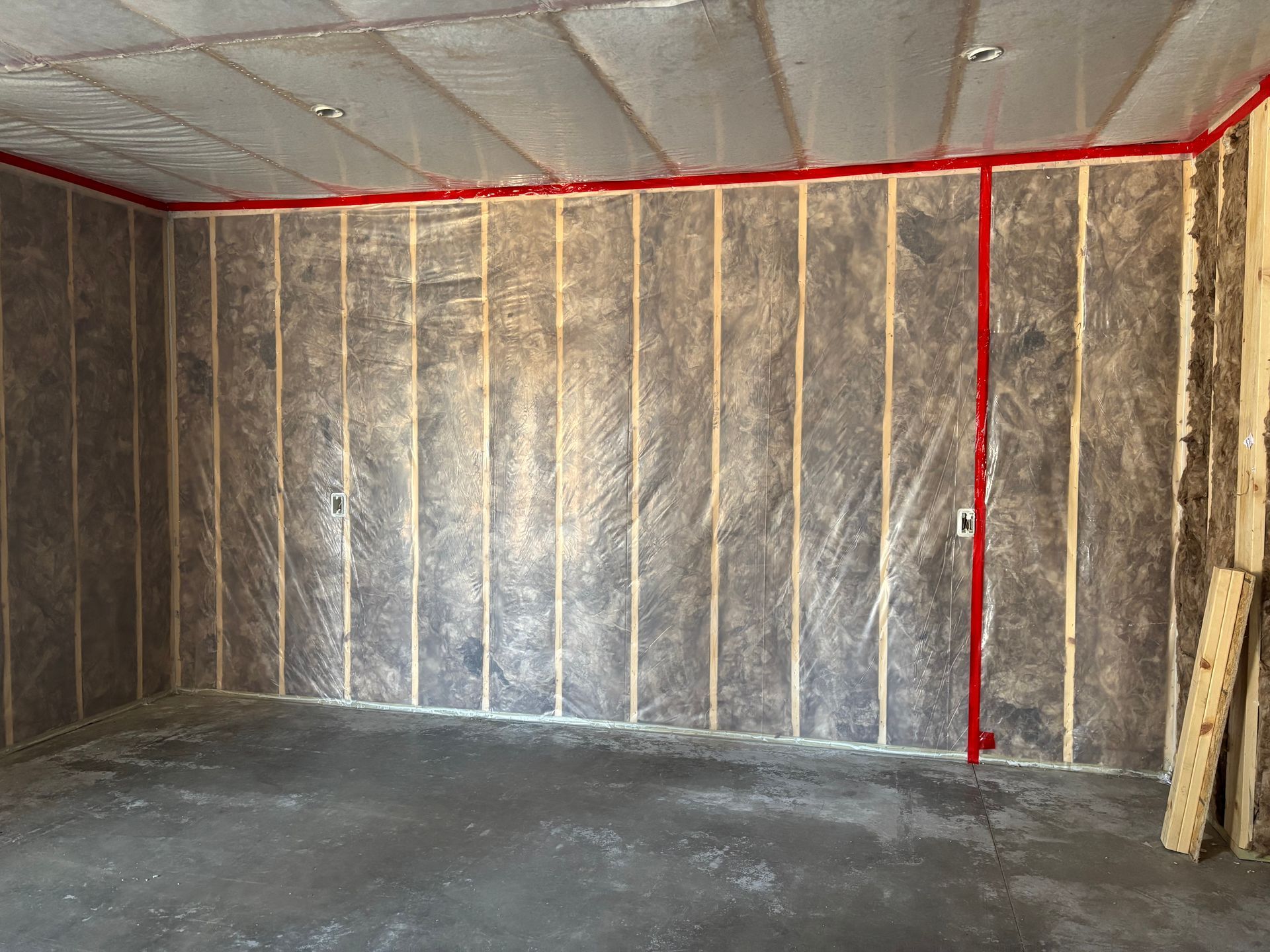 Insulation being installed in the walls and ceiling of a wooden frame house under construction.