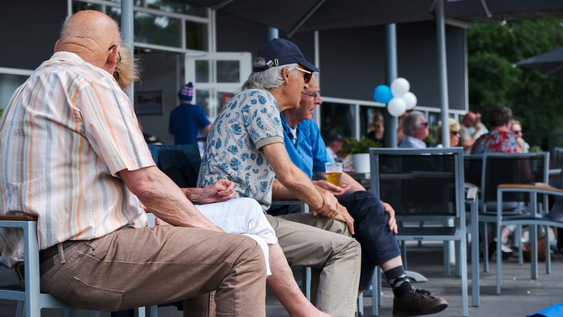 Een groep mensen zit buiten op een terrasje, te kletsen en te genieten van een drankje in een ontspannen buitenomgeving.