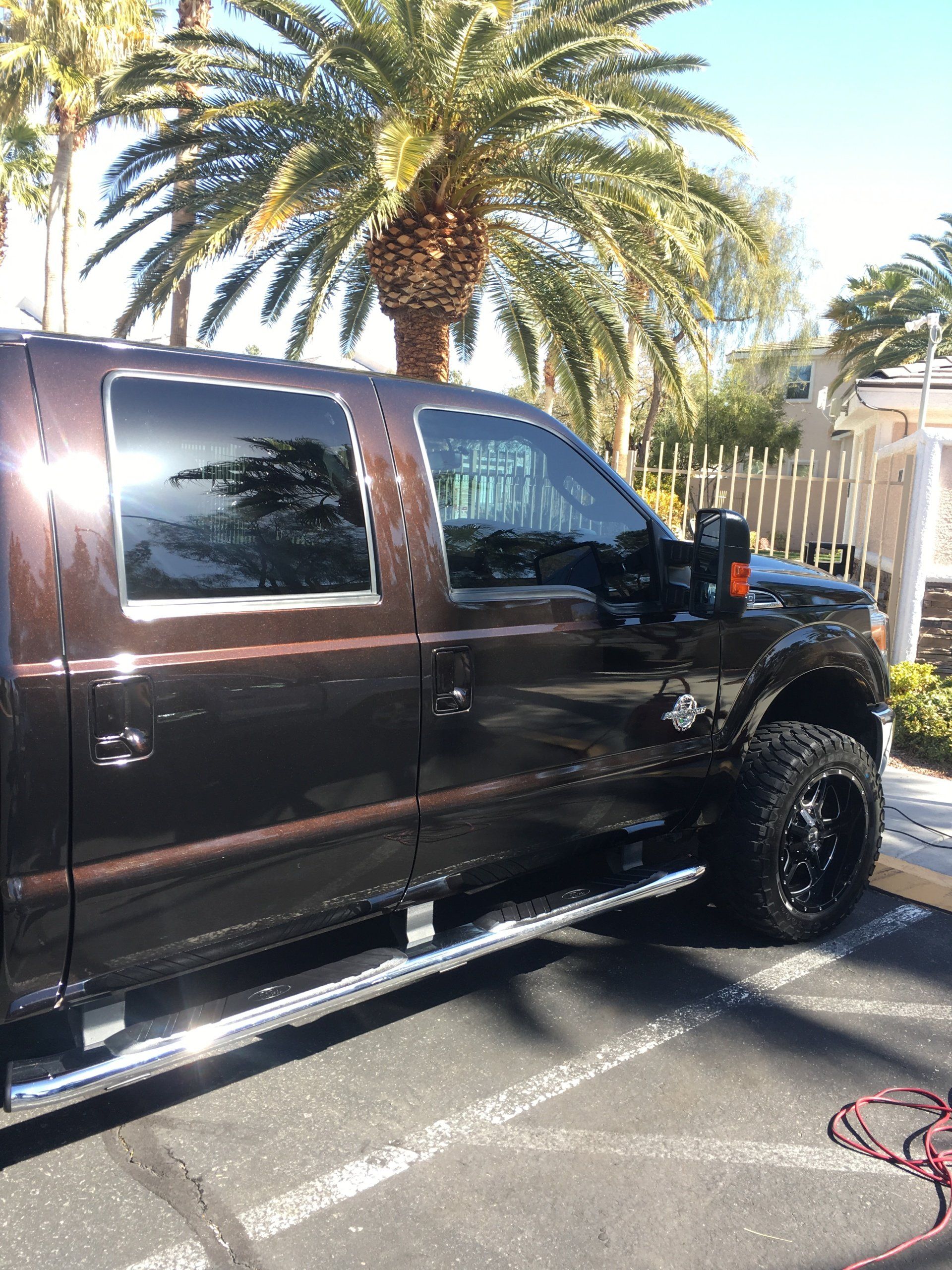 A brown truck is parked in a parking lot next to a palm tree.