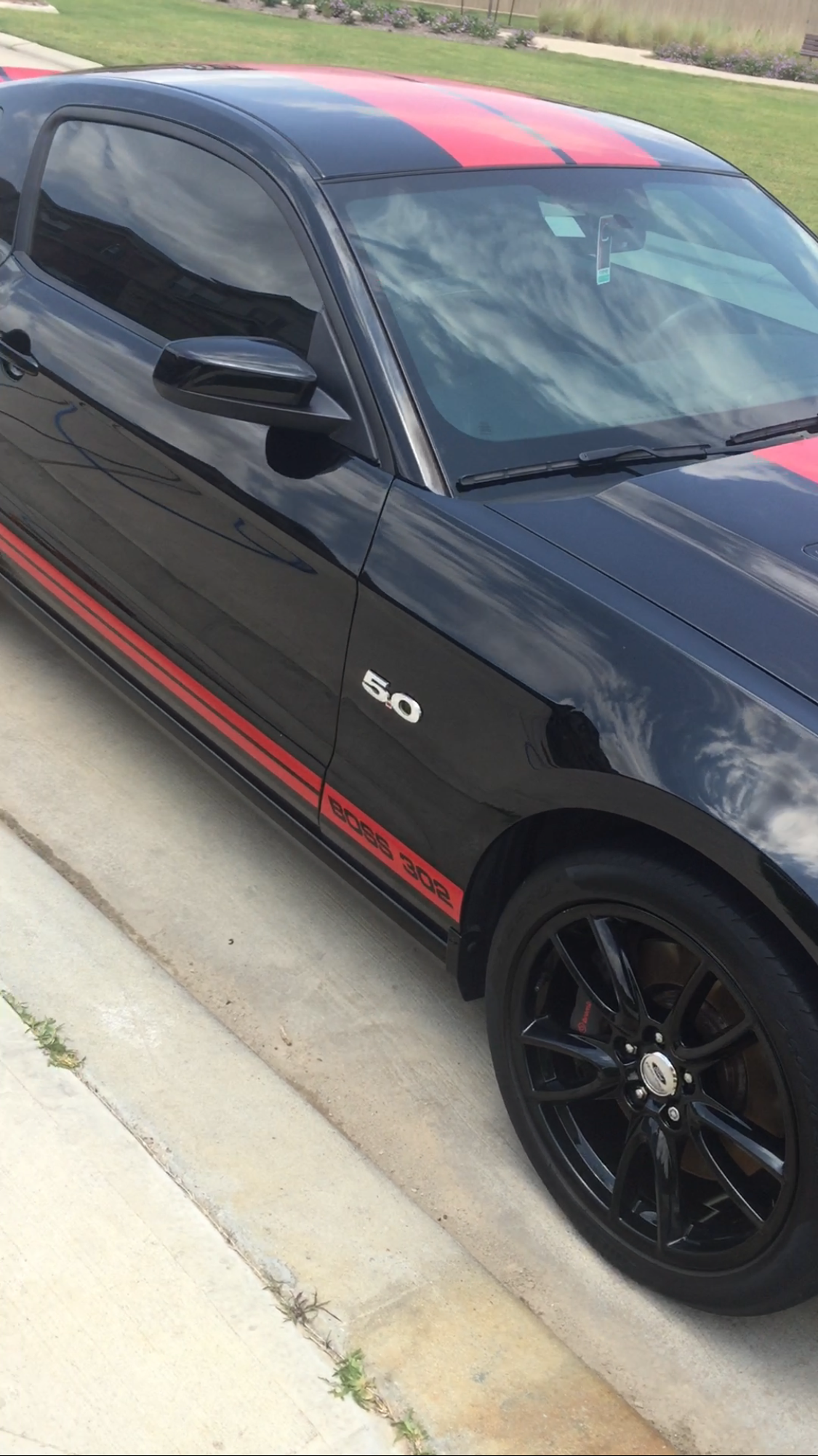 A black and red mustang is parked on the side of the road.