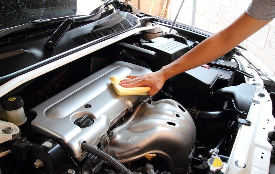 A person is cleaning the engine of a car with a cloth.