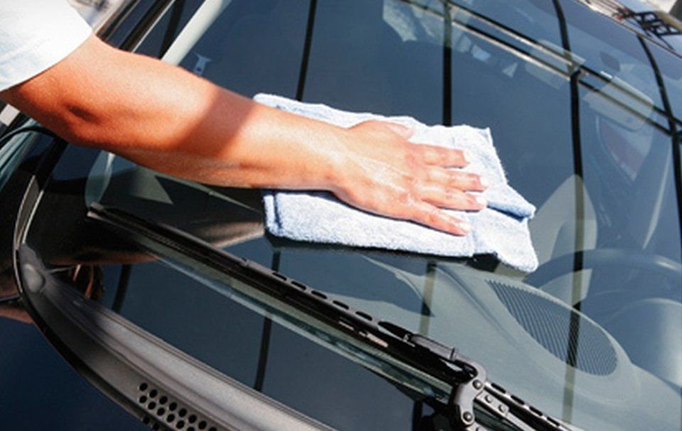 A person is cleaning a car windshield with a towel