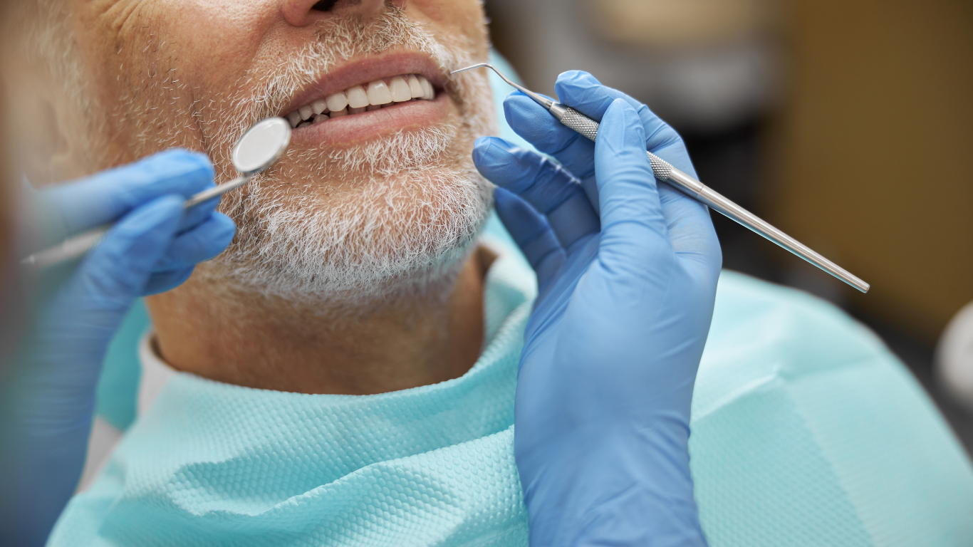 Dentist examining patient's teeth with tools; hands in blue gloves, patient in blue bib.