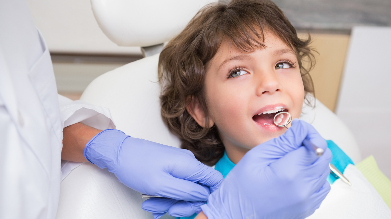 Child at the dentist with mouth open. Dentist examining with a mirror. Wearing blue gloves, in an office.
