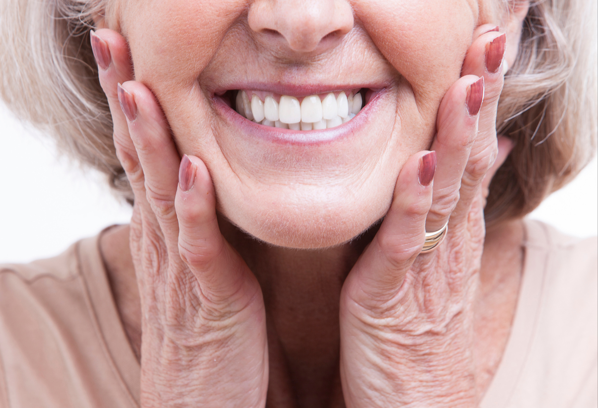 Woman with hands framing her smiling face, showing a bright, healthy smile.