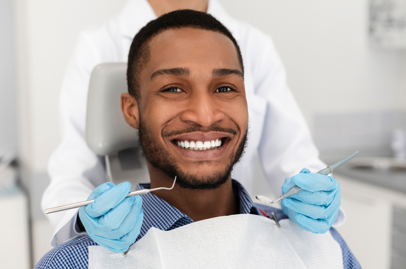 Man smiling at the dentist, holding dental tools, wearing a bib, blue gloves.