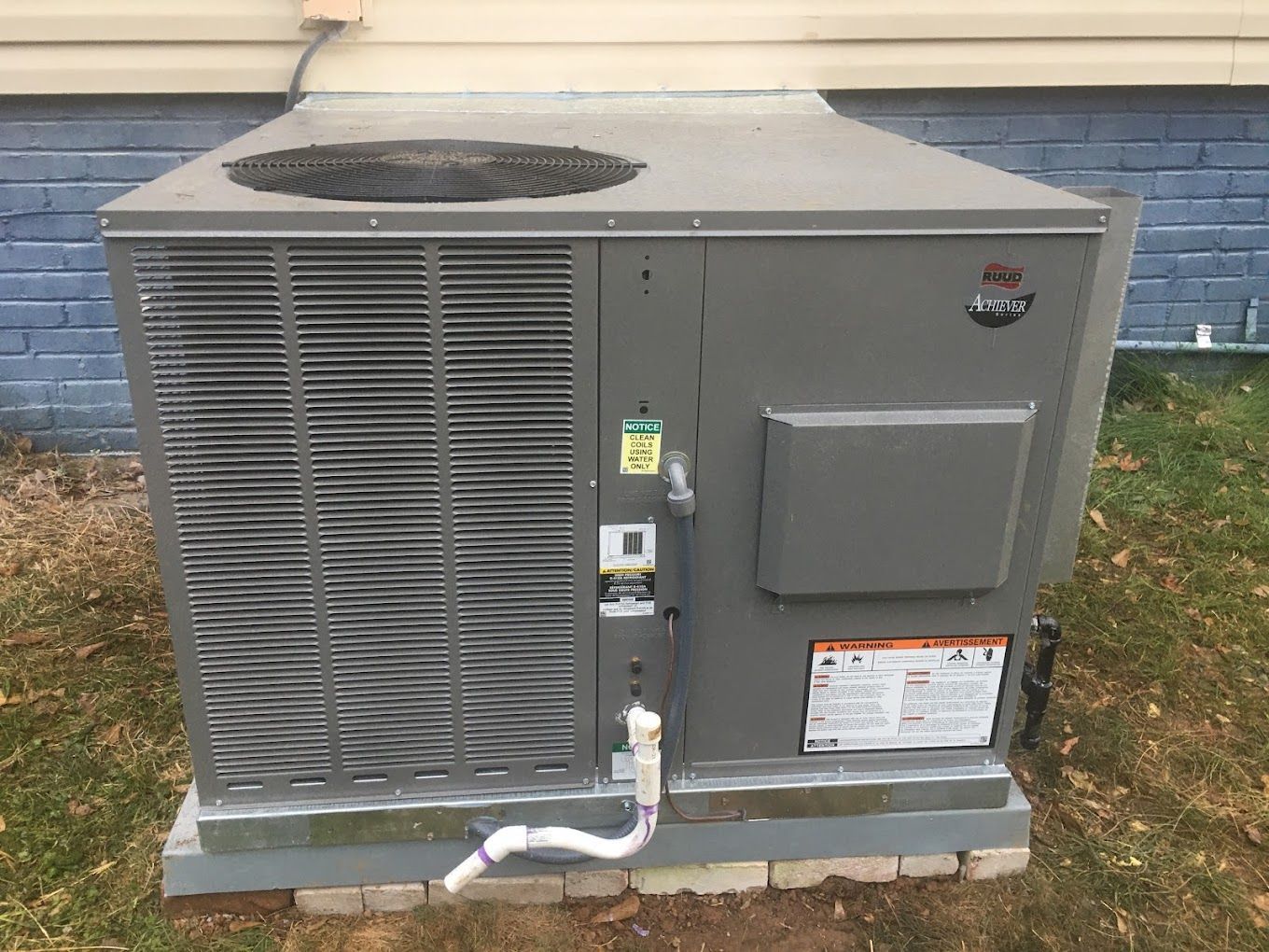 A large air conditioner is sitting outside of a brick building.