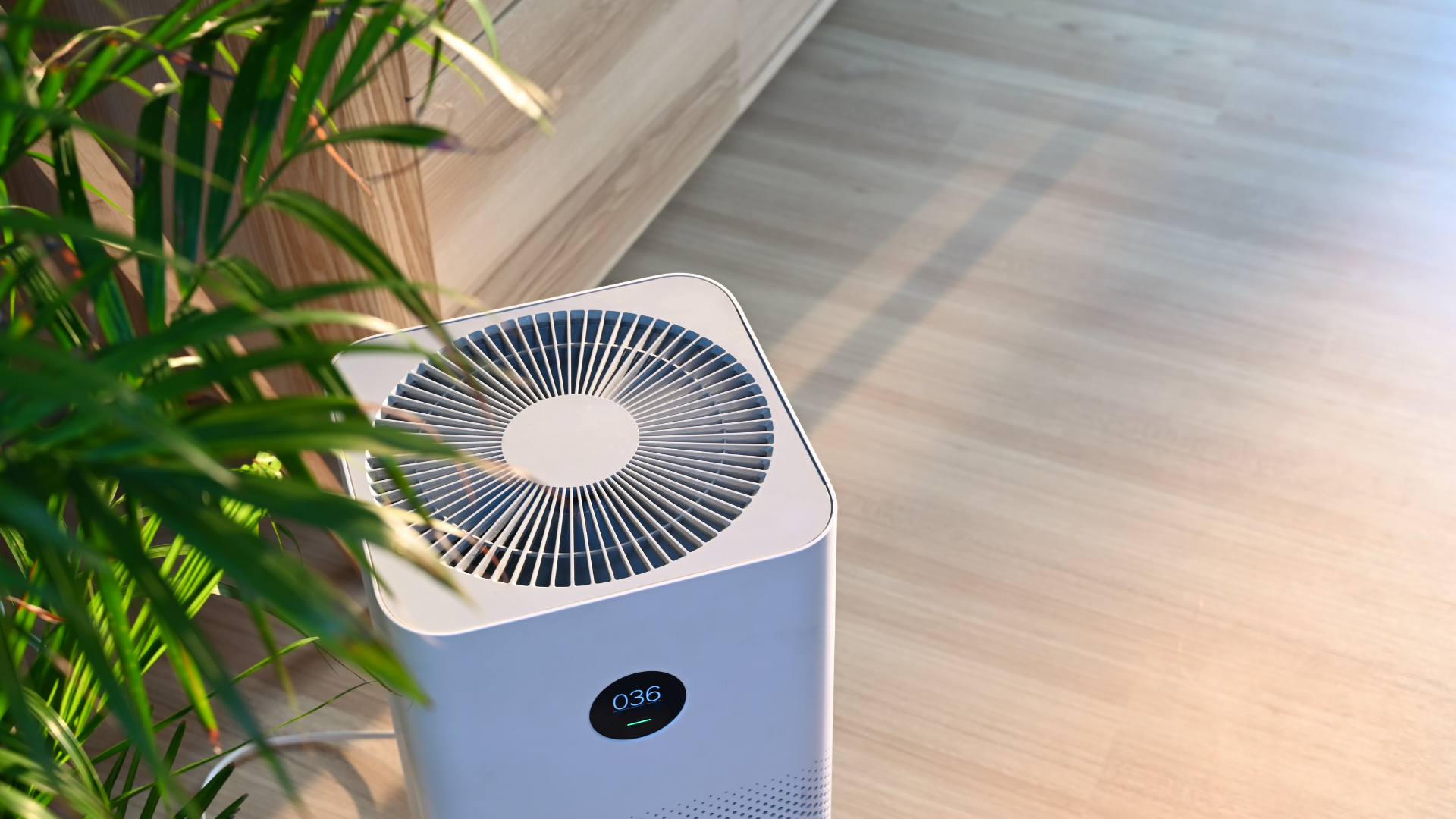 A white air purifier is sitting on the floor next to a plant.