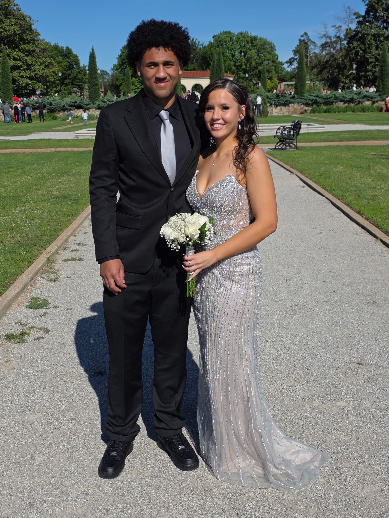 Couple posing on a garden path, the woman holding a bouquet and wearing a silver gown.
