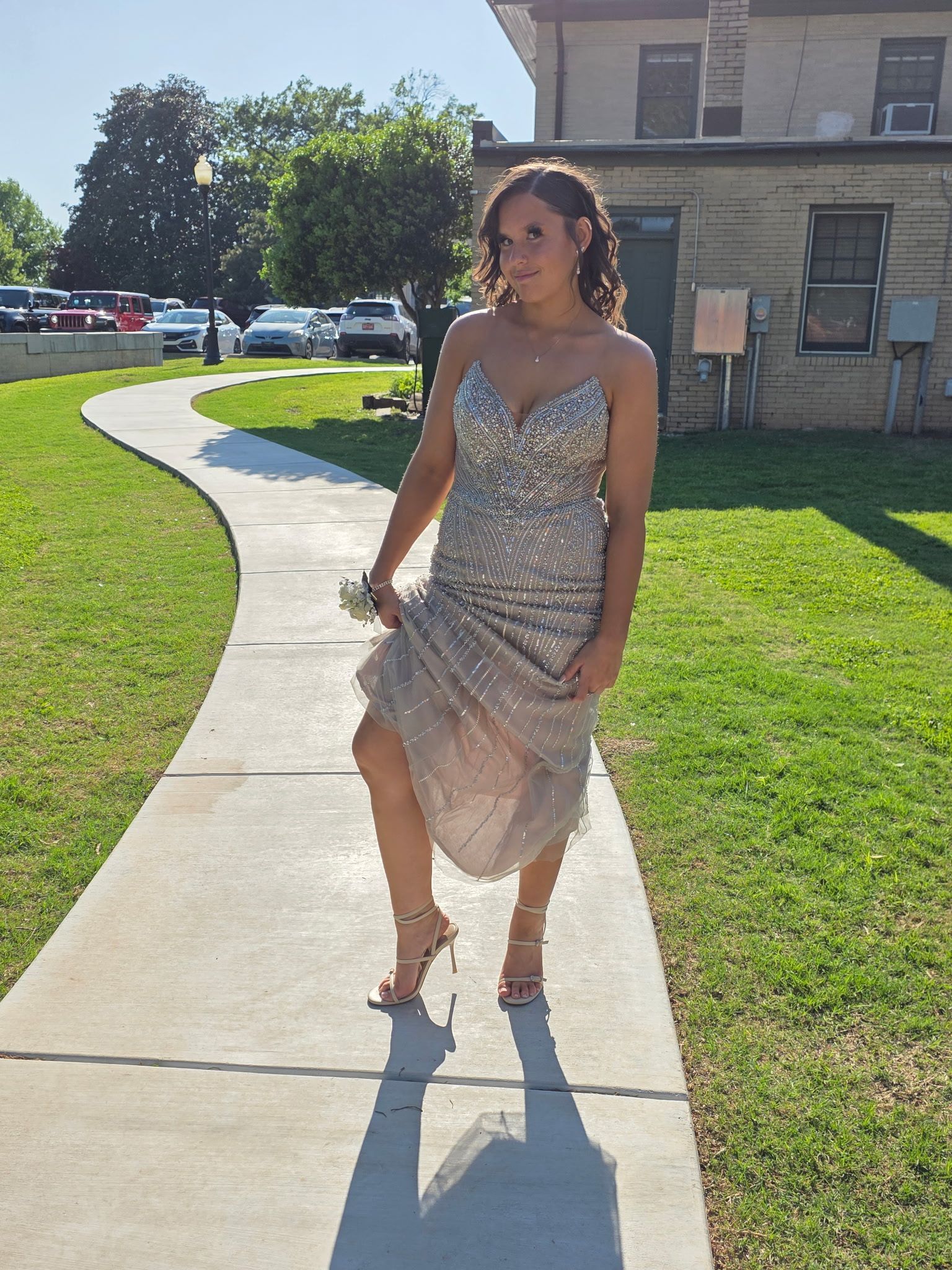 Woman in a sparkly silver dress standing on a sunlit sidewalk outside a building