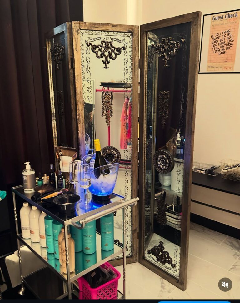 A salon station with a mirrored screen, bottles, and an ice bucket holding a bottle.