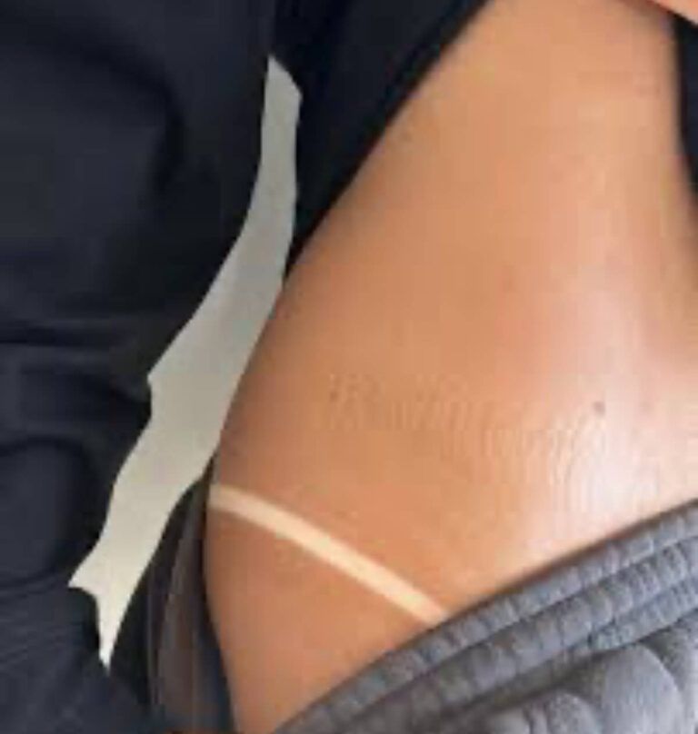 Close-up of a person's torso showing a stark tan line from clothing. Tan skin, gray pants, dark upper clothing.