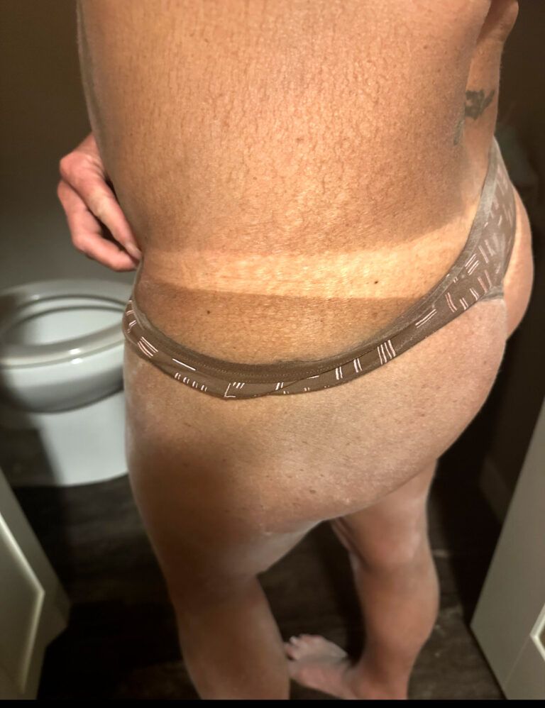 Person with tan lines from underwear in a bathroom, revealing fair skin below tan.