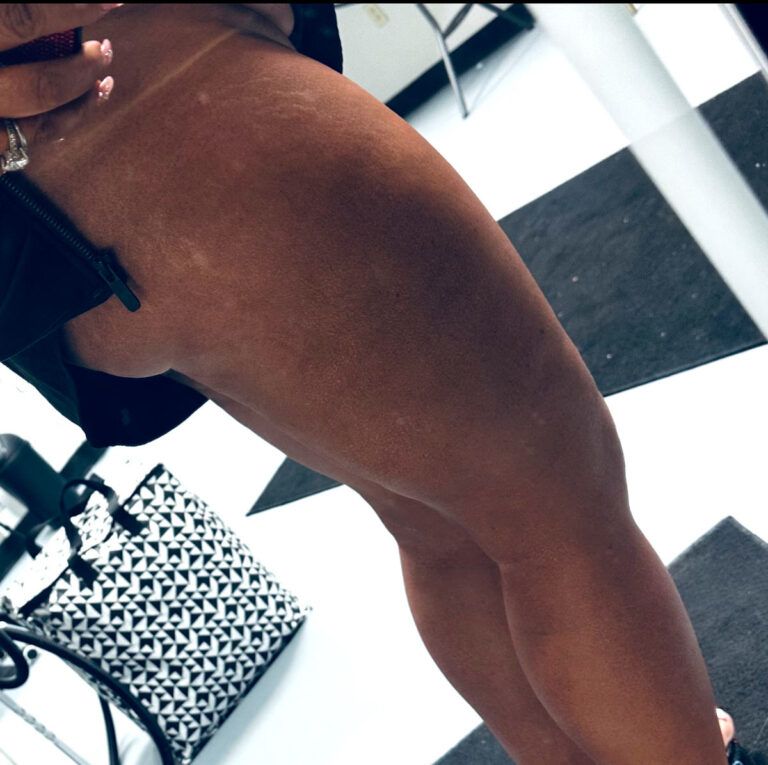 Darkly tanned leg, with clothing partially visible. White and black tiled floor, mirror reflection.