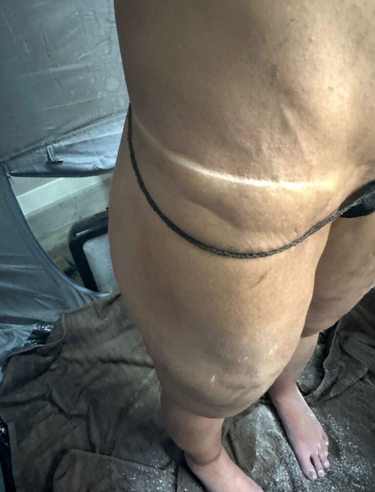 Leg and torso with a tan line, standing near a towel and equipment.