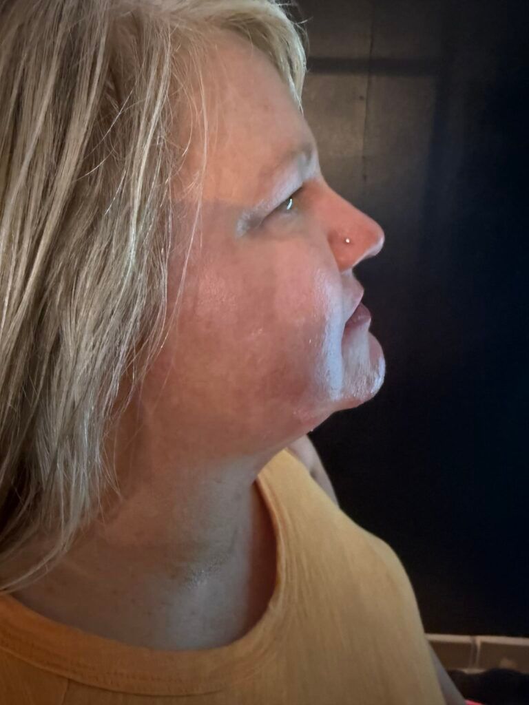 Woman in profile, looking up, nose ring visible, wearing orange shirt, against dark background.