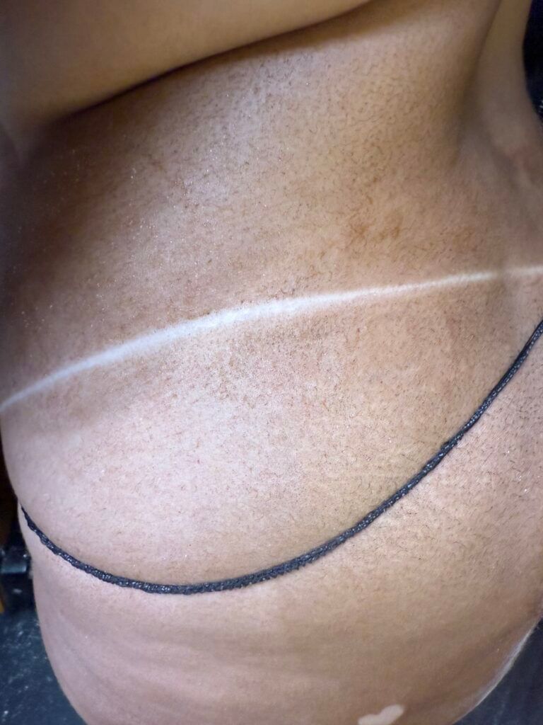 Torso with tan line across the chest and a dark chain around the waist.