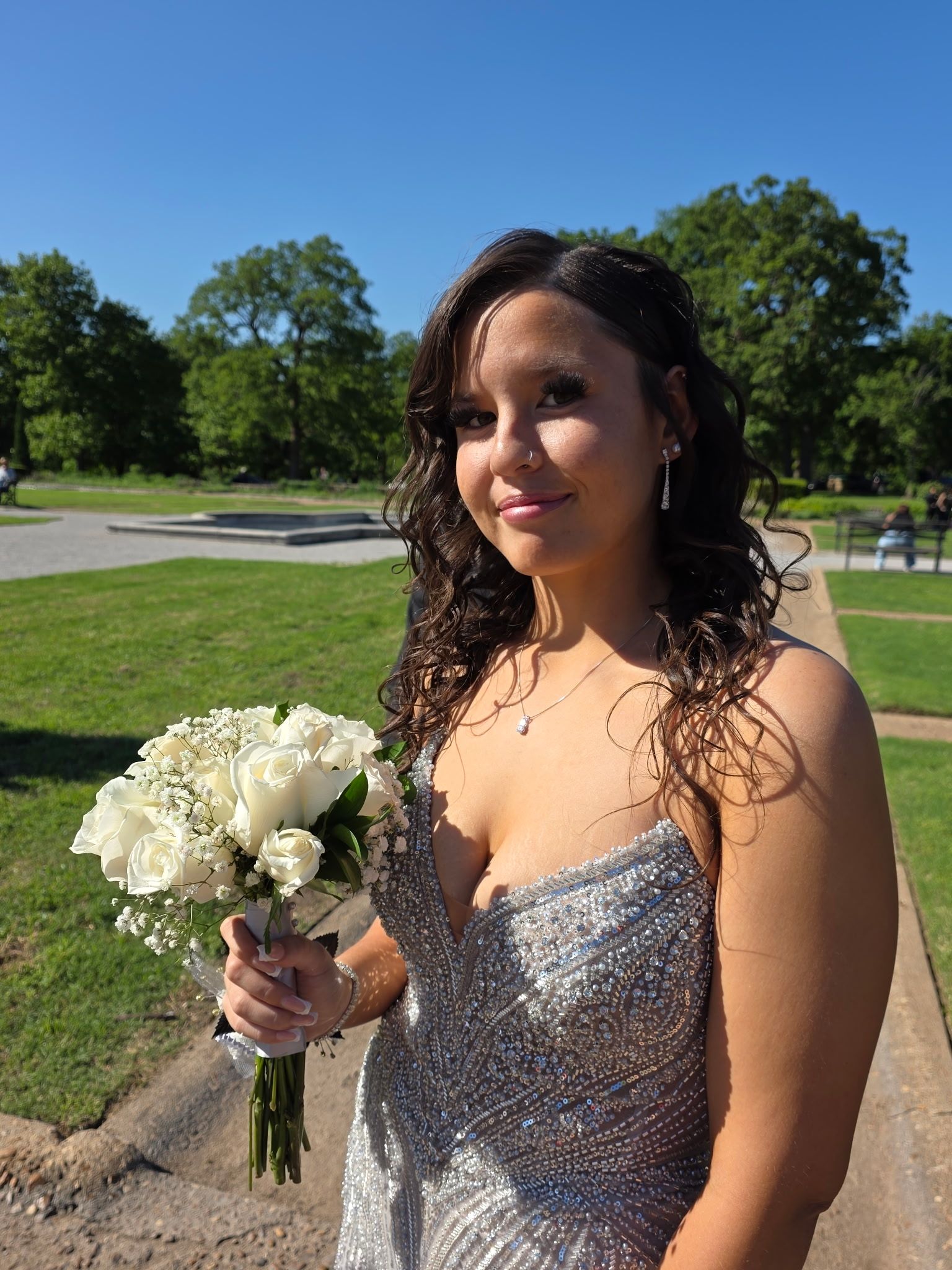 Woman in a silver dress holding a white bouquet outdoors on a sunny day