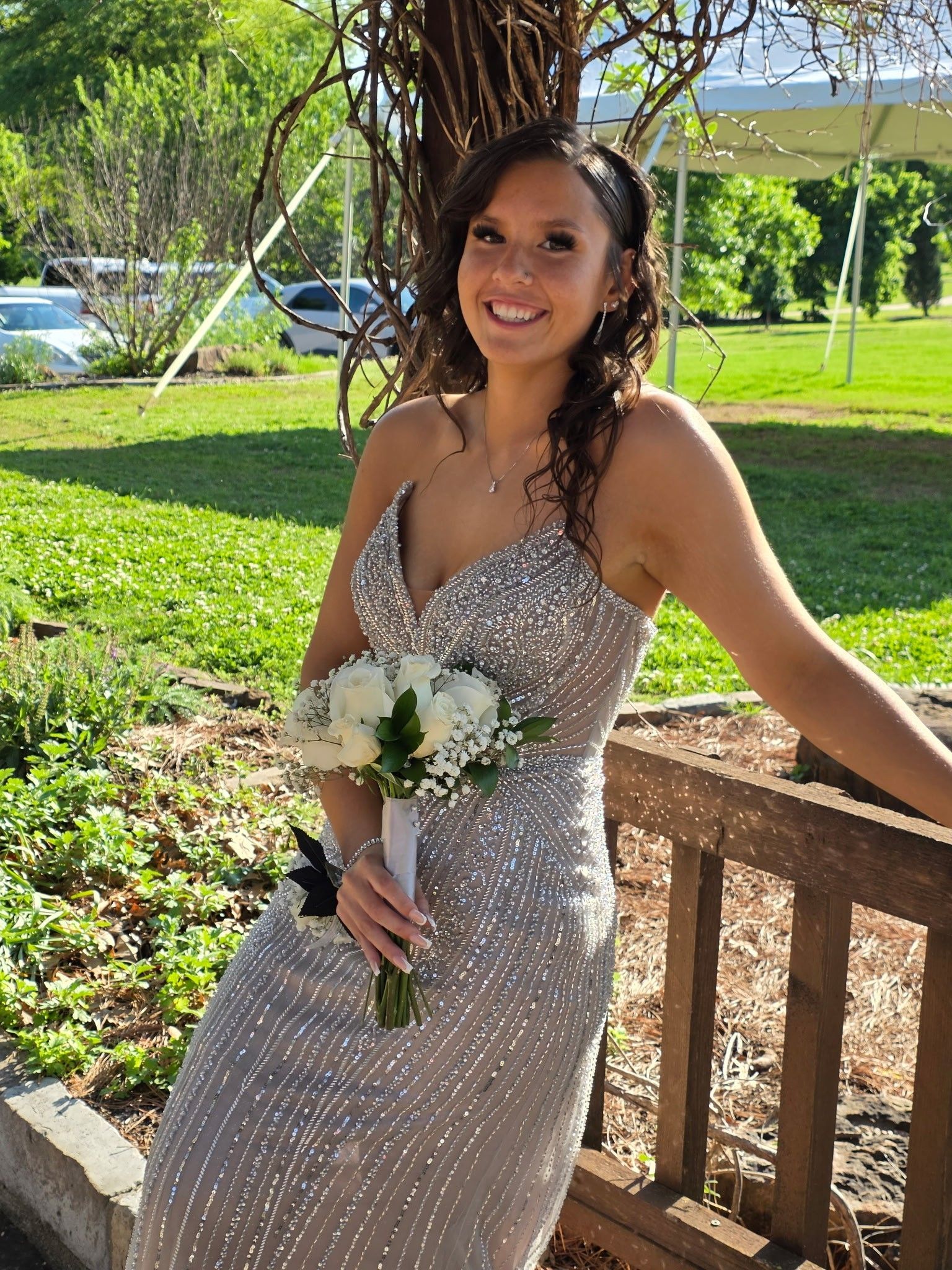 Woman in a sparkly dress holding a bouquet, smiling on a porch in a sunny garden