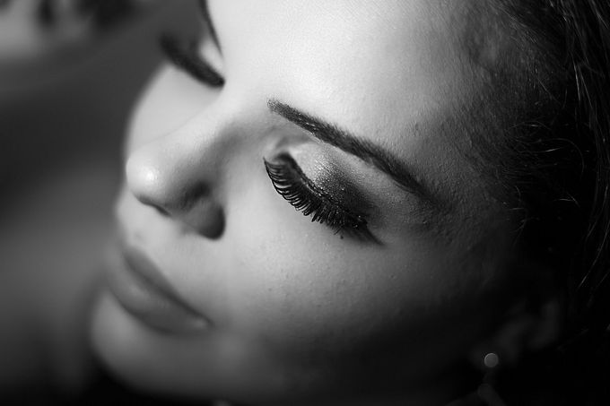 Person receiving eyelash extensions. Technician in pink gloves applies adhesive with a wand; eye area protected by pads.