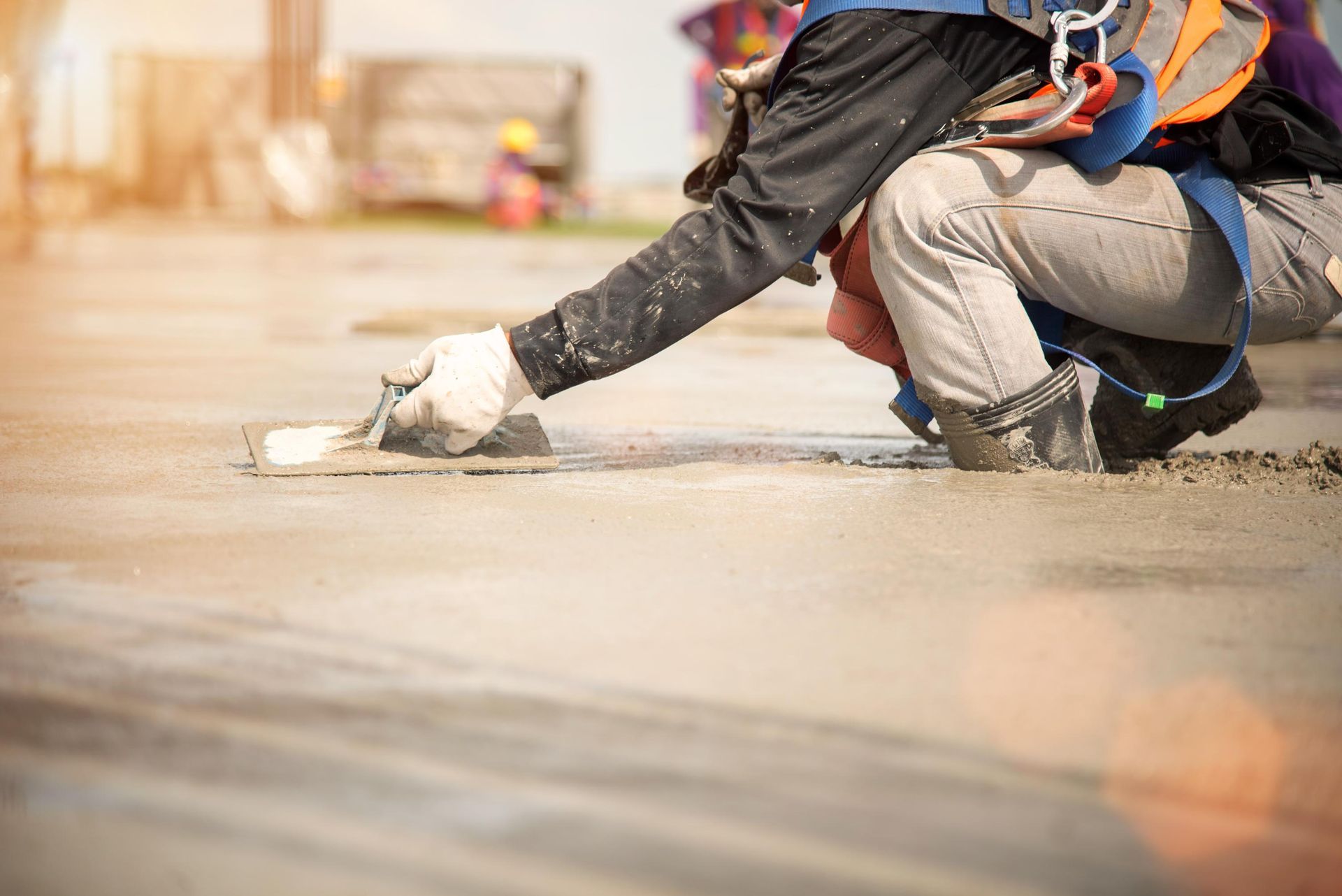a construction worker is kneeling down and spreading concrete on the ground .