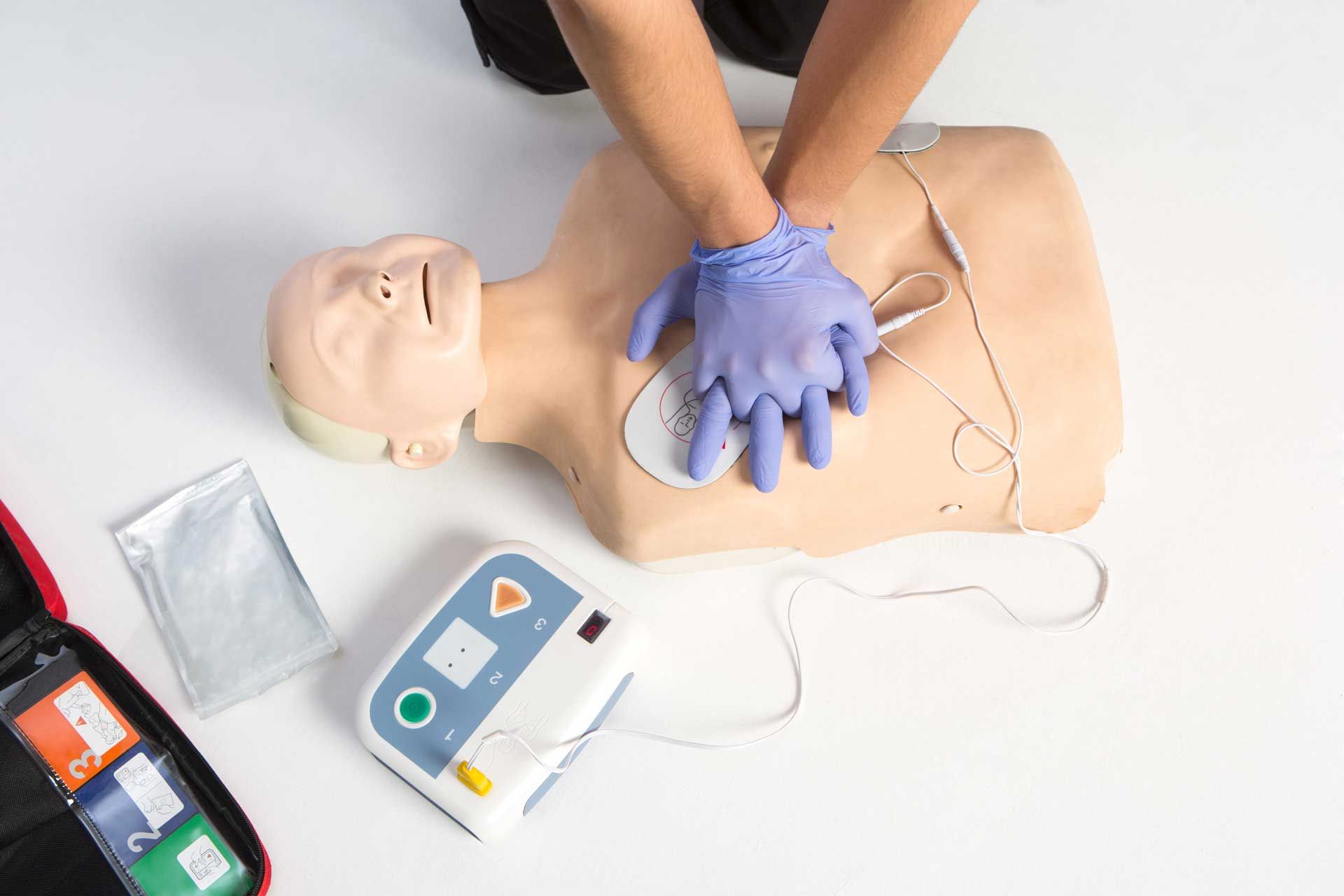 Person performing CPR on a mannequin, with an attached AED and supplies.