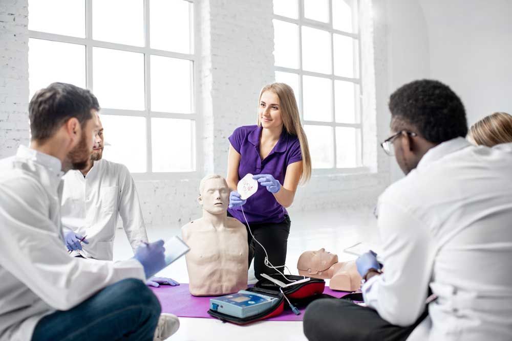 CPR training: instructor showing device to a group of diverse people with manikins in bright room.