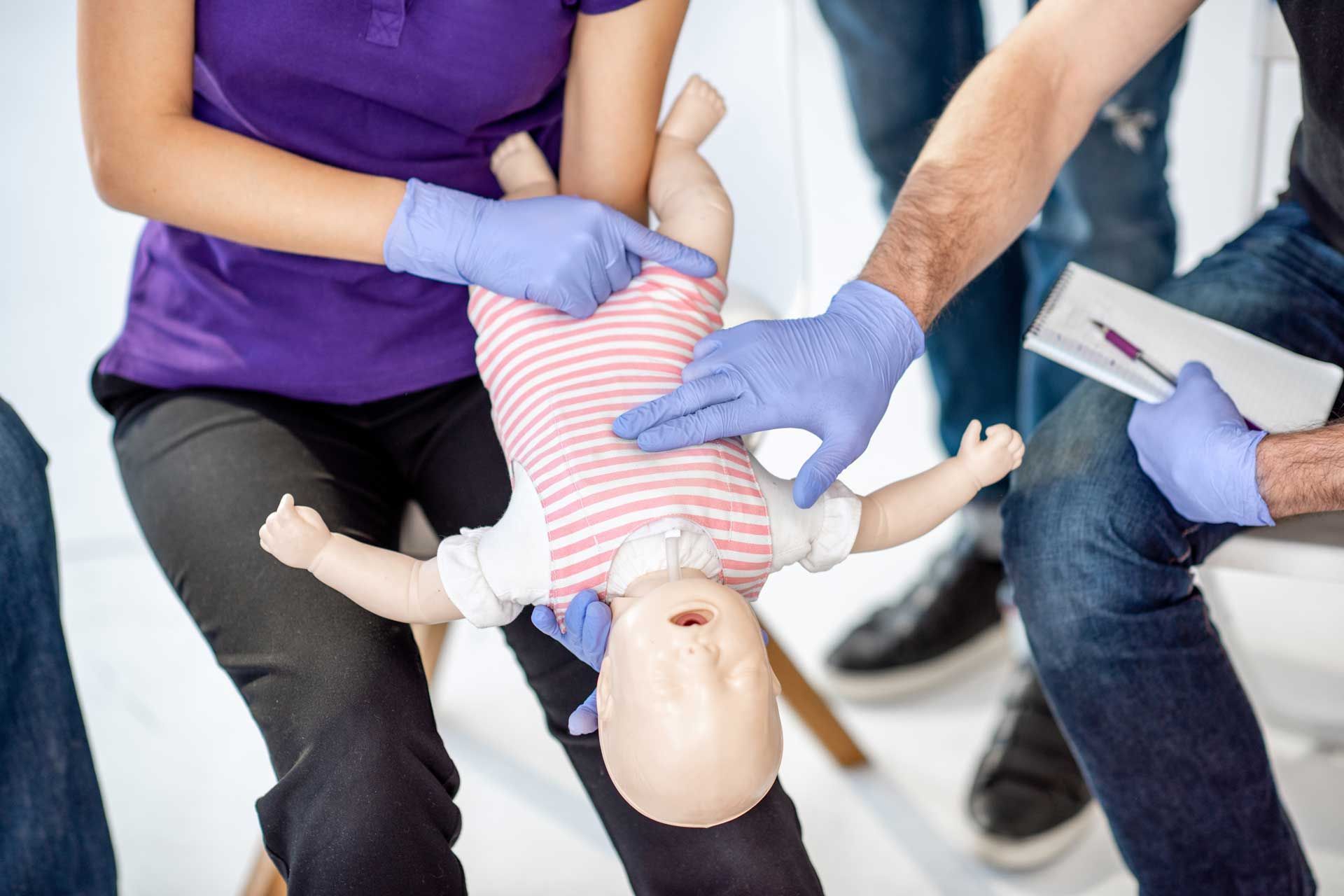 CPR training: Instructor demonstrating abdominal thrusts on baby mannequin.