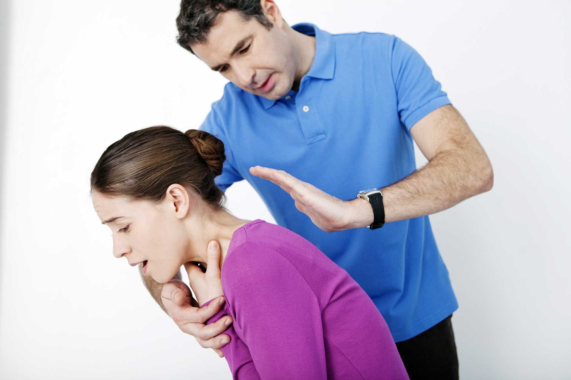 Man performing the Heimlich maneuver on a woman; she clutches her throat, leaning forward.